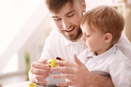 Father painting Easter eggs with his child at tableの写真素材