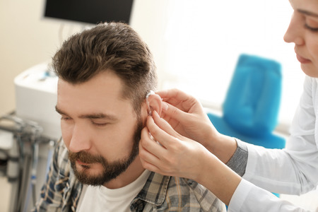 Otolaryngologist putting hearing aid in man's ear in hospitalの写真素材