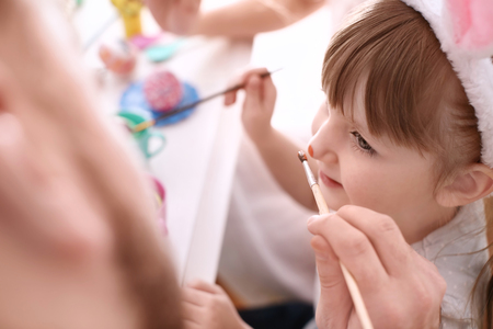 Father painting Easter eggs with his daughter at tableの写真素材