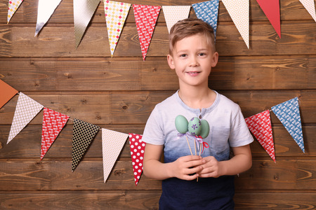 Cute little boy holding Easter eggs near wooden wall decorated with party pennantsの写真素材
