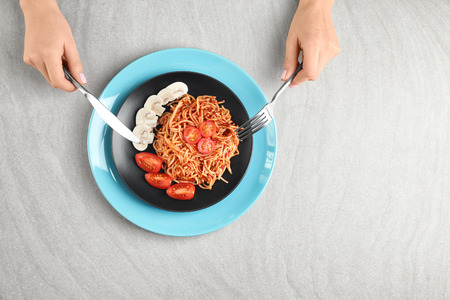 Woman eating delicious pasta with mushrooms and tomato sauce at tableの写真素材