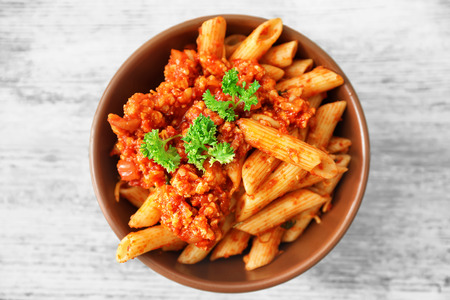 Bowl with tasty penne pasta and bolognese sauce on wooden tableの写真素材