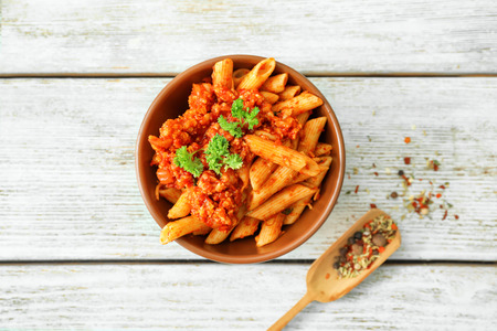 Bowl with tasty penne pasta and bolognese sauce on wooden tableの写真素材