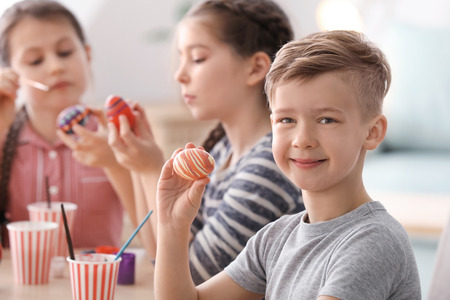 Cute little boy and his friends painting eggs for Easter at homeの写真素材