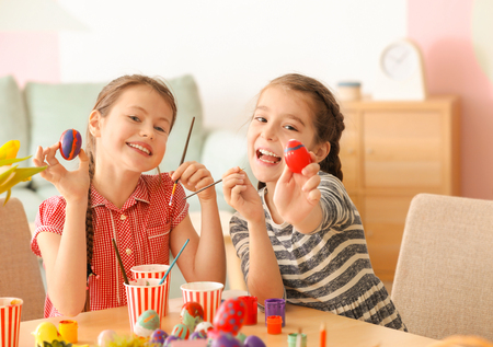 Cute little girls painting eggs for Easter at tableの写真素材