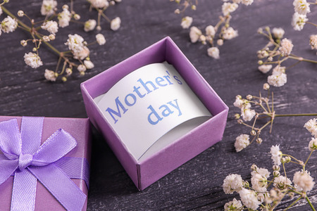 Card with phrase Mother's day in gift box and flowers on table