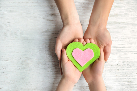 Hands of mother and child with felt heart on wooden backgroundの写真素材