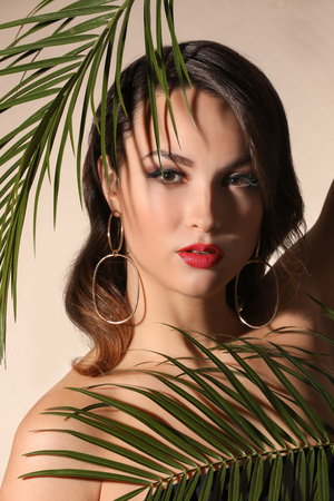 Portrait of young woman with beautiful professional makeup and palm leaves on light backgroundの写真素材