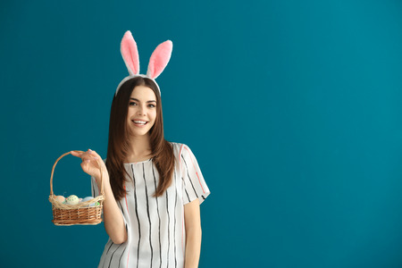 Beautiful young woman with Easter eggs and bunny ears on color background
