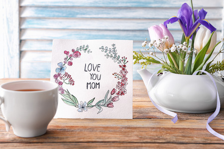 Card with words LOVE YOU MOM, cup of tea and flowers on table. Mother's day celebrationの写真素材