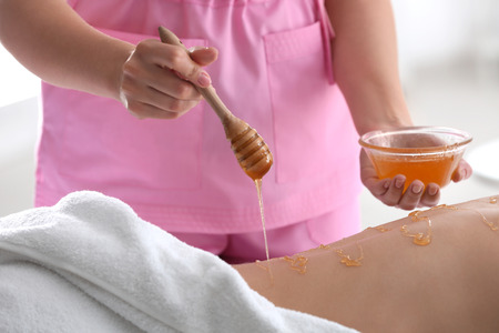 Female masseur using honey for spa procedure in salonの写真素材