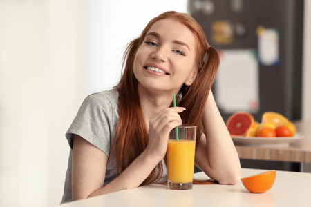 Beautiful young woman drinking citrus juice in kitchenの写真素材