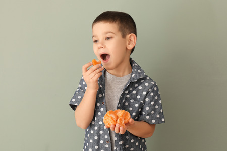Funny little boy eating citrus fruit on color backgroundの写真素材