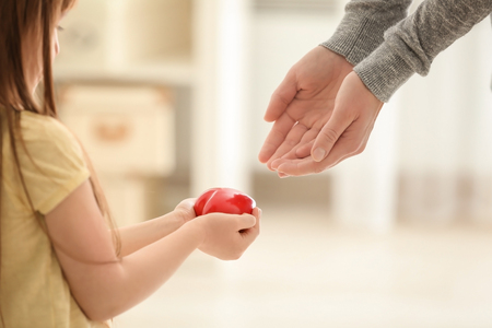 Little girl giving red heart to her mother on blurred backgroundの写真素材