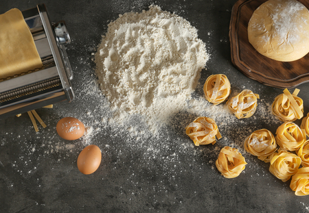 Metal pasta maker with dough and products on kitchen table, top view