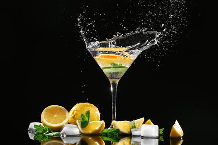 Glass of splashing cocktail and slices of citrus fruits on black backgroundの写真素材