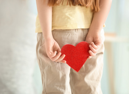 Little girl hiding red heart for mother behind back, closeupの写真素材