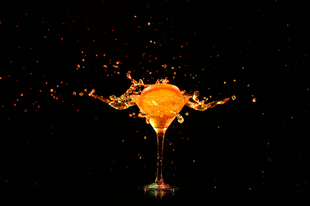 Glass with splashing cocktail and slice of citrus fruit on black backgroundの写真素材