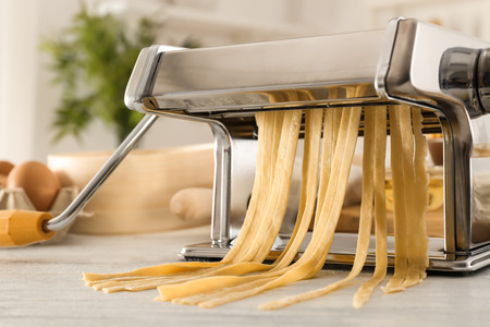 Metal pasta maker with dough on kitchen tableの写真素材