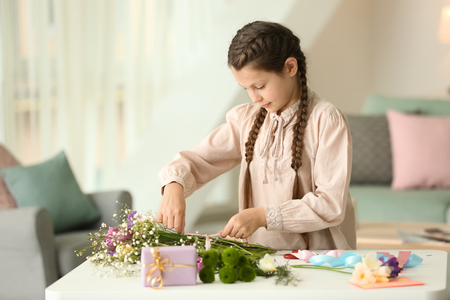 Little girl preparing bouquet of flowers for mother at homeの写真素材