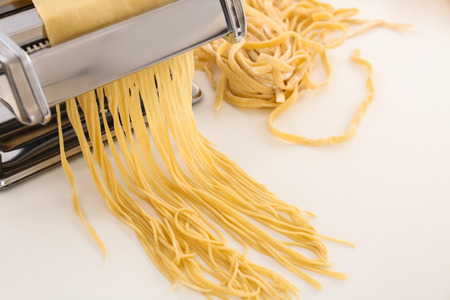 Metal pasta maker with dough on white backgroundの写真素材