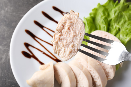 Fork with piece of boiled chicken fillet over plate, closeupの写真素材