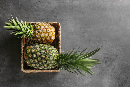 Wicker basket with fresh ripe pineapples on grey backgroundの写真素材
