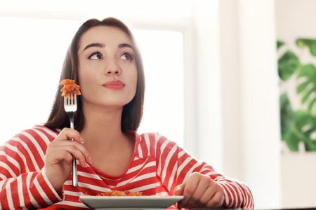 Young woman eating delicious pasta indoorsの写真素材