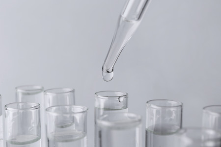 Pipette dripping sample into test tube on light background, closeup