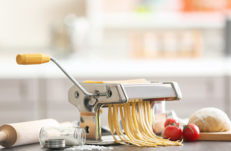 Making tagliatelle with pasta machine on table in kitchenの写真素材