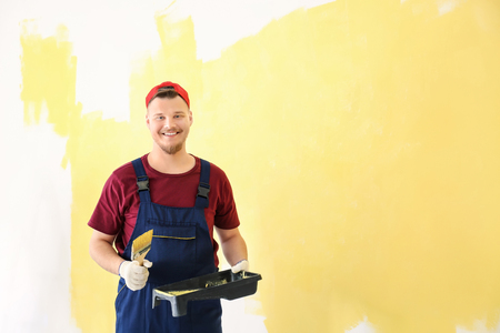 Male decorator in uniform with brush and paint tray on color backgroundの写真素材