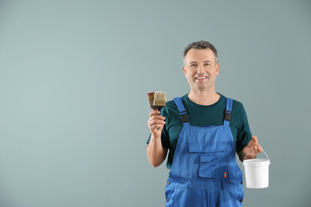 Male painter in uniform with brushes and bucket of paint on color backgroundの写真素材
