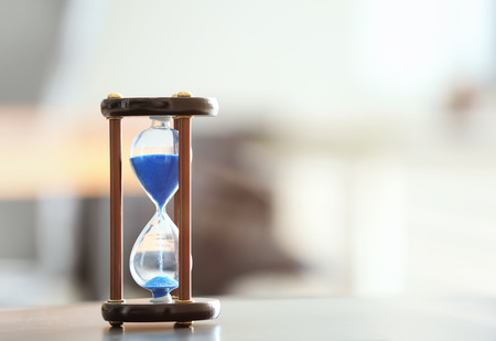 Hourglass on table against blurred background. Time management concept