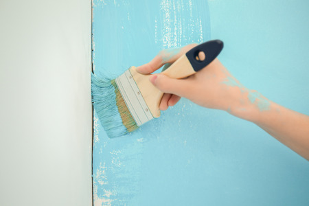 Female painter using brush for refurbishing color of wall indoors