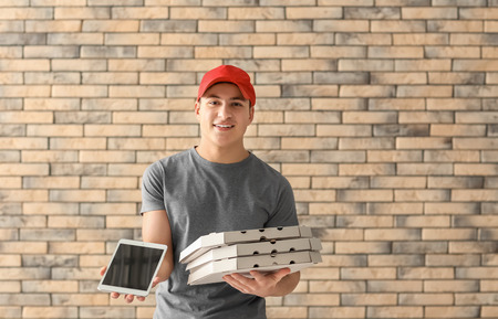 Delivery man with cardboard pizza boxes and tablet on brick wall backgroundの写真素材