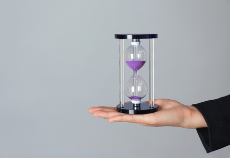 Female hand holding hourglass on gray background. Time management conceptの写真素材