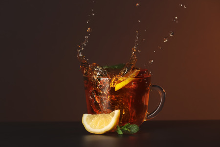 Glass cup and splash of delicious lemon tea with mint on table against color backgroundの写真素材