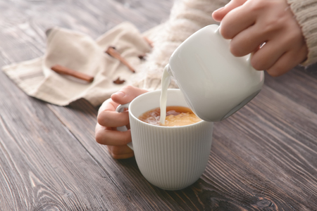 Woman pouring milk into cup of tea on tableの写真素材