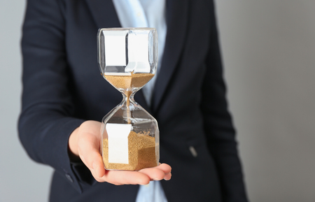 Woman holding sand hourglass on gray background. Time management concept