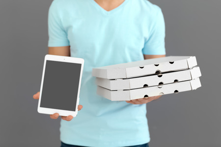 Delivery man with cardboard pizza boxes and tablet on grey background
