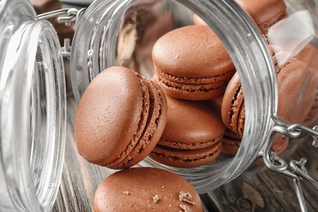 Glass jar and delicious chocolate macarons on tableの写真素材