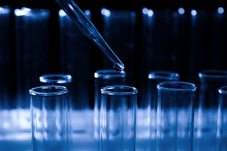Pipette dripping sample into test tube on dark background, closeup