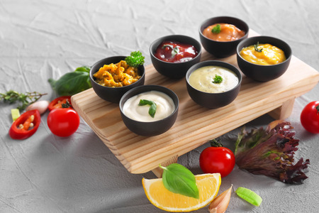 Different tasty sauces in bowls on wooden board