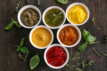 Different tasty sauces in bowls with herbs on wooden tableの写真素材