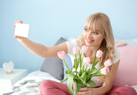 Young woman taking selfie with tulip bouquet in bedroomの写真素材