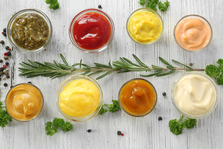 Different tasty sauces in bowls with spices on white wooden table