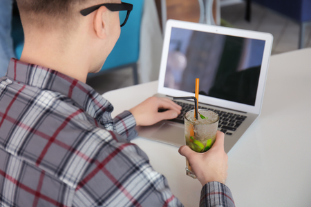 Young freelancer drinking cocktail while working with laptop at table in cafeの写真素材