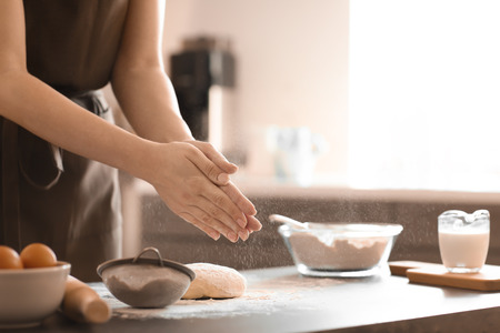 Baker sprinkling flour on dough at tableの写真素材
