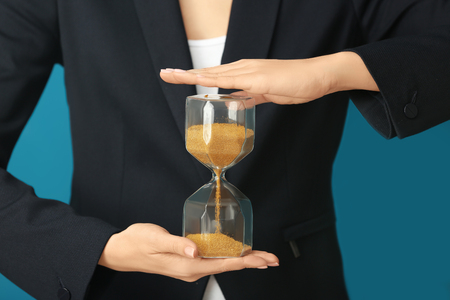 Woman holding hourglass on color background, closeup. Time management concept