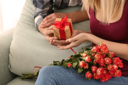 Young man giving present to his beloved girlfriend at home, closeupの写真素材